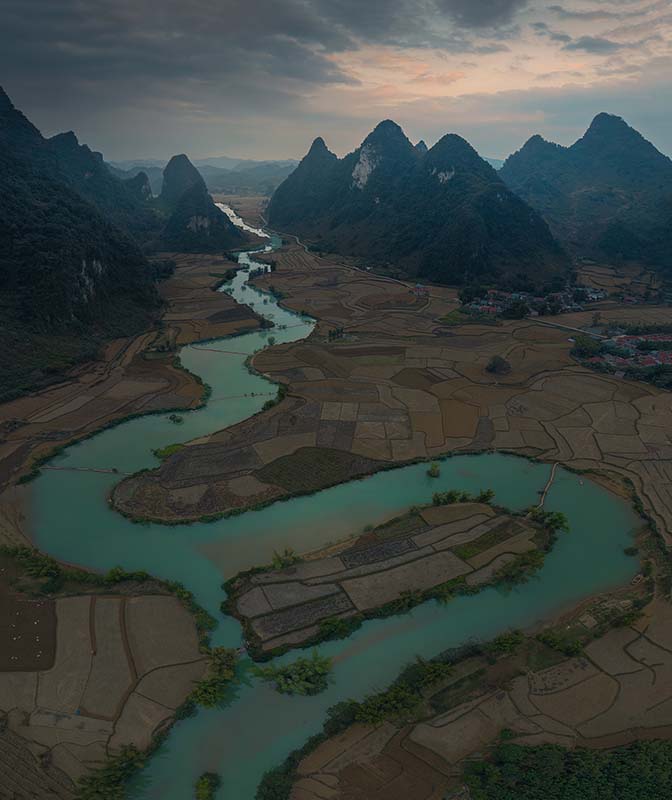 an ultra blue river winders through dome shaped mountains as seen by drone in north Vietnam at sunrise.