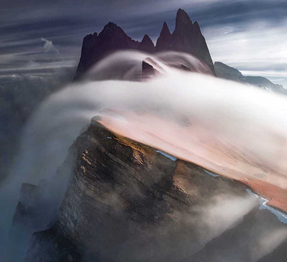 Seceda mountain peaks in the dolomites at sunrise with incredible misty and clouds rolling over the peaks.