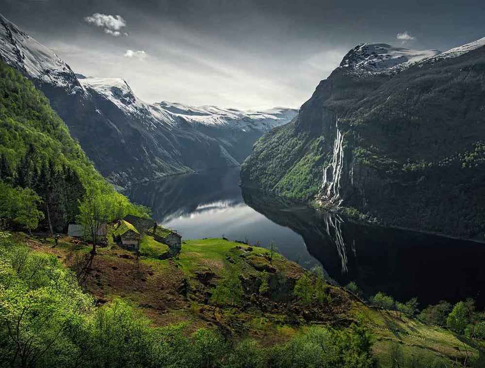 geiranger fjord in Norway from a green hillside overlooking several old farm houses and the seven sisters waterfall across the fjord.