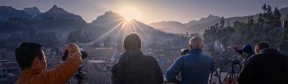 Sunrise in Huaraz from the rooftop view. A sunstar in the middle of the mountains. Four photographers stand shooting the mountain.