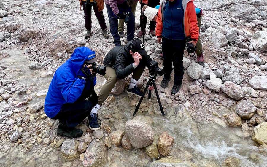 Max Rive stands in a small stream surrounded by clients as he sets up a long exposure using a tripod. 