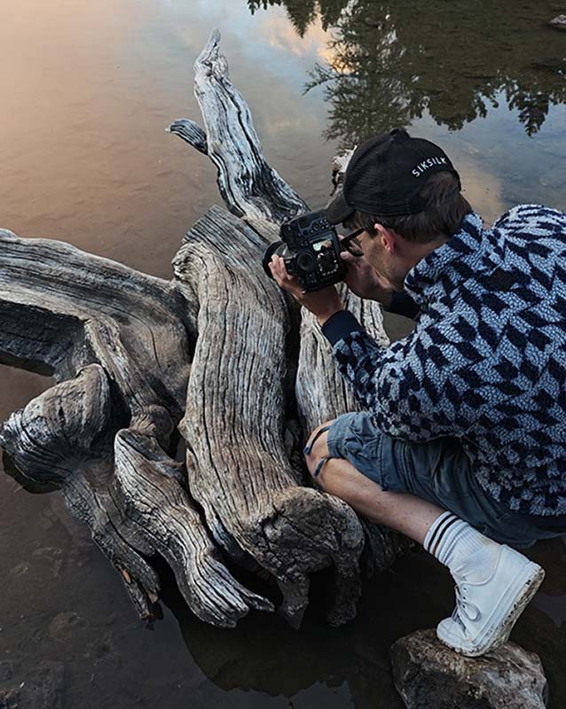 max rive uses his leg and elbow as a tripod whilst photographing leading lines in a tree trunk in dolomites in summer.