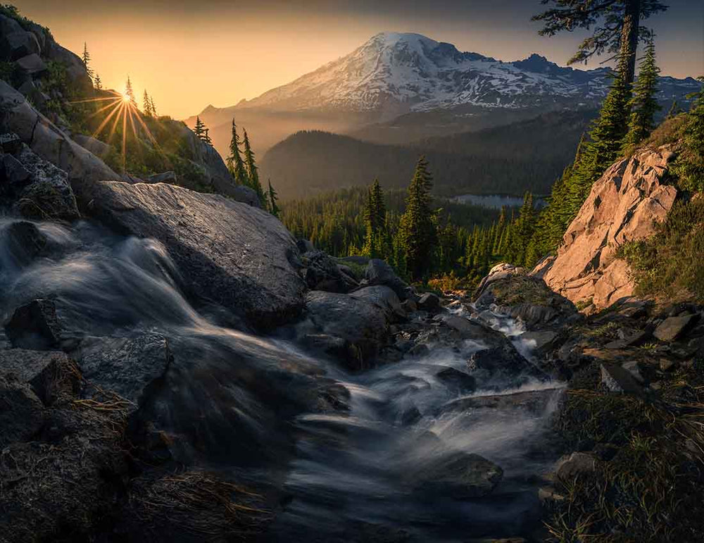 a waterfall on a mountain during golden sunrise and stunstar with a view of forest and snowy mountain in USA.