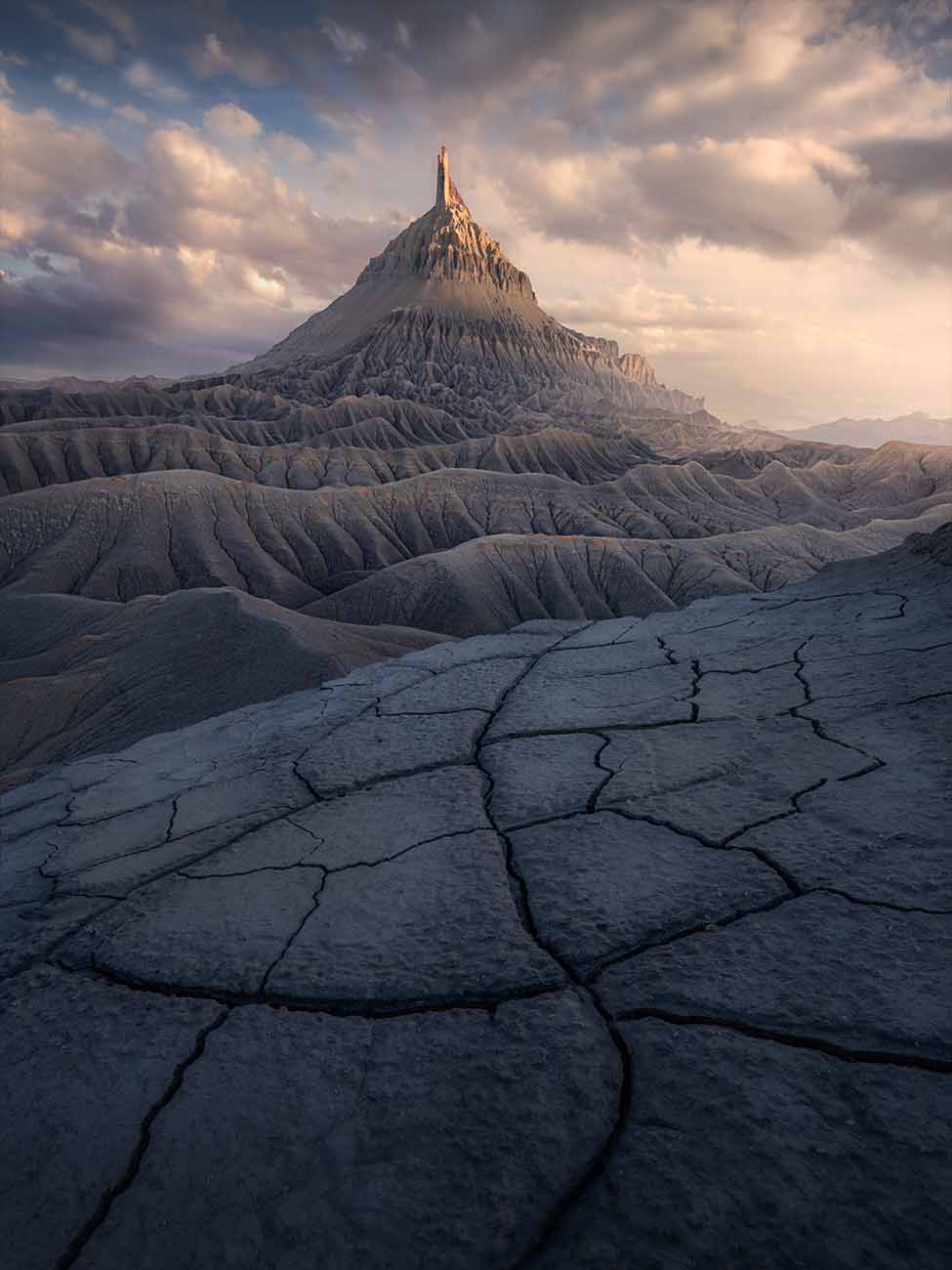 Factory butte at sunset in golden light winter time. Giant cracks of mud creating leading lines to the mountain.
