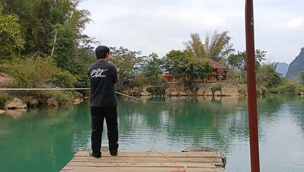 a man uses a rope to pull a driftwood passenger raft across a small blue lake in north Vietnam to the hotel on the opposite shore.