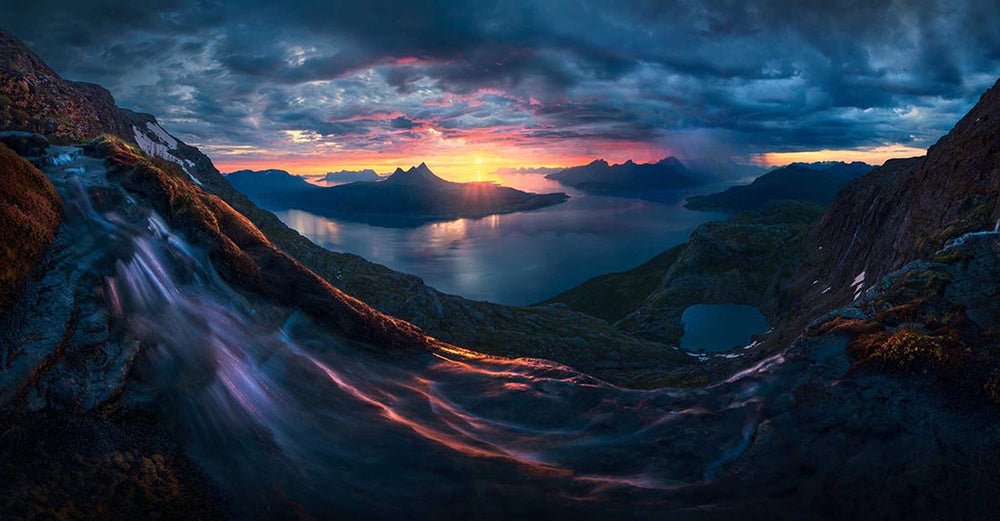 a large waterfall in Evenes Norway at sunset with coloured sky and fjords in the background.