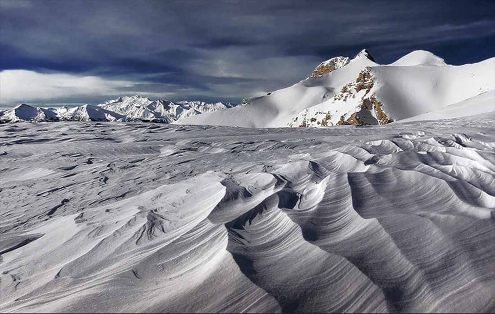 Snow patterns high in the French Alps during winter creating lines and soft formations beneath the sharp snowy mountains.