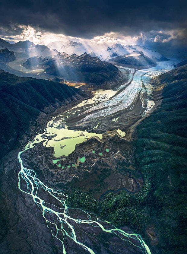aerial view above a glacier with rivers and forest - background lightrays and mountains - patagonia 