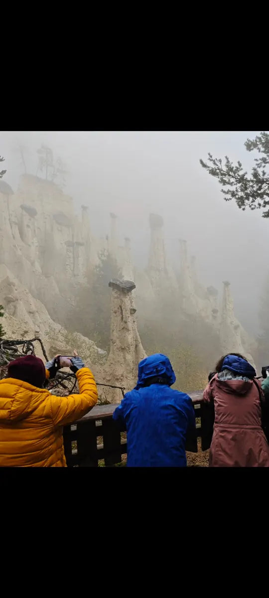 Photographers in colourful jackets looking at rock pillars in the mist