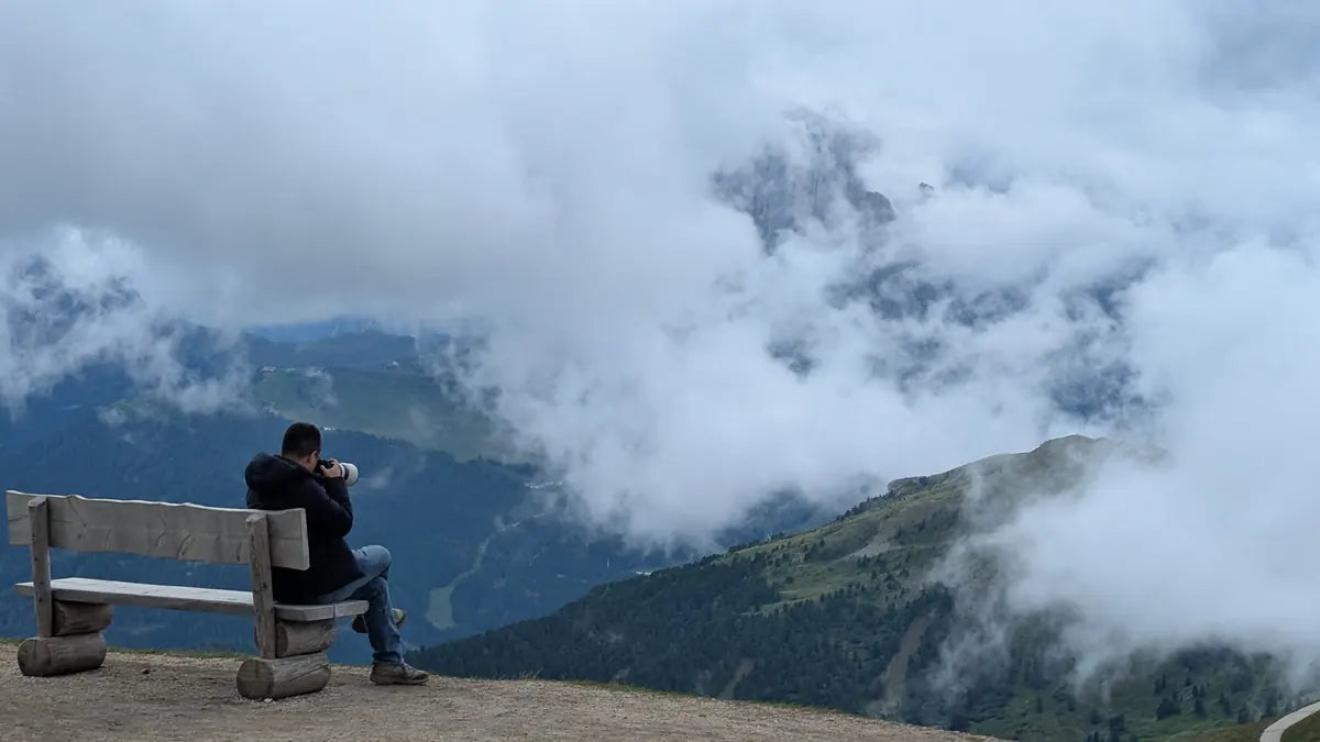 A person sitting on a wooden bench overlooking clouds drifting through a mountain valley in the Dolomites