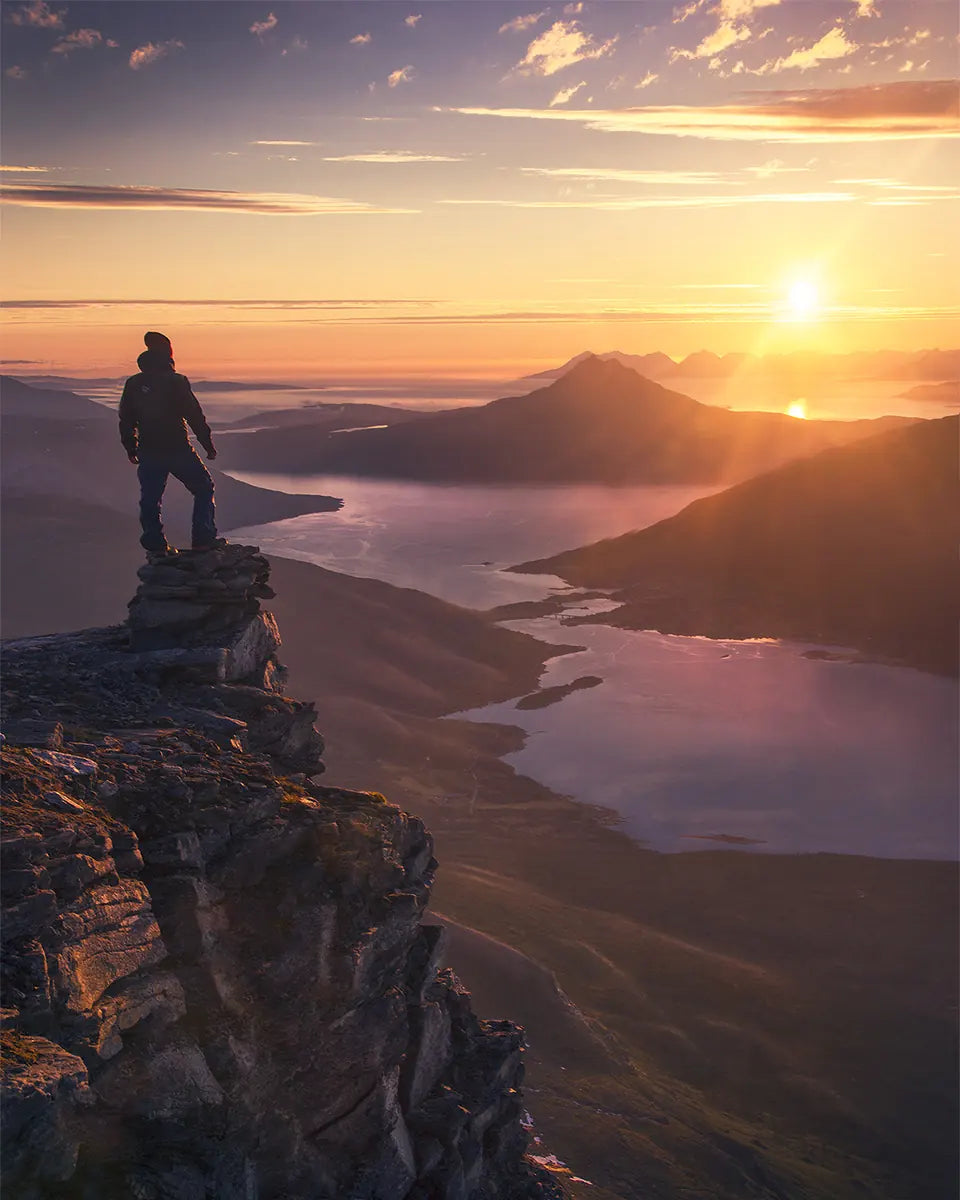 A person standing on a rocky ridge above winding waterways in golden evening light