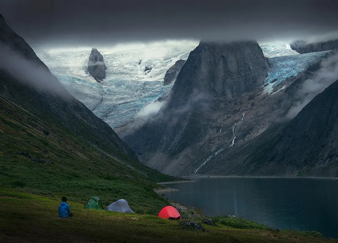 Tents beside a still mountain lake beneath steep cliffs and a glacier