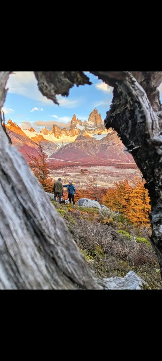 Two people among autumn trees below Fitz Roy, viewed through an opening in a tree trunk