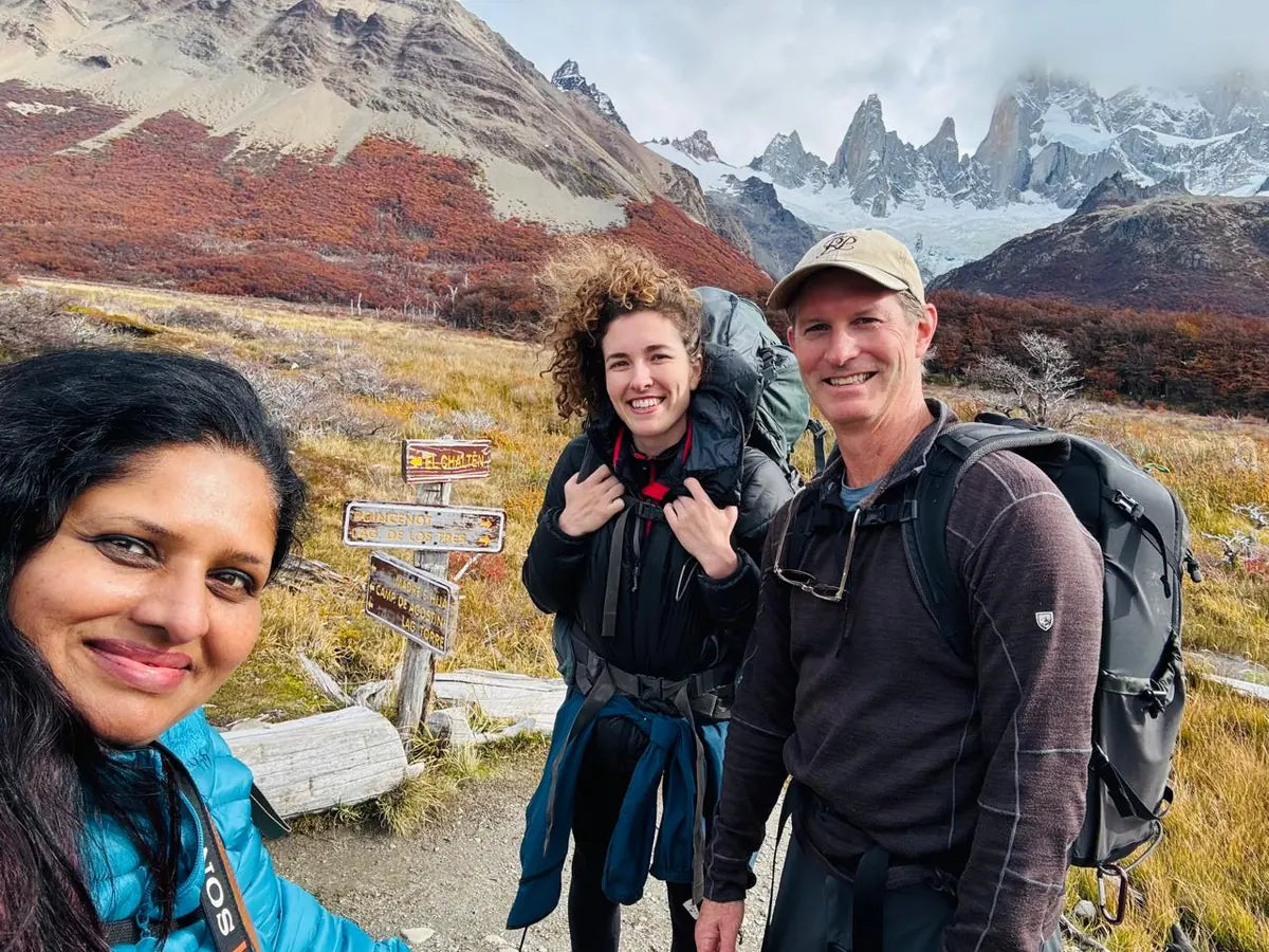 Three smiling hikers with backpacks beside a trail sign, autumn forest and mountain peaks in Patagonia