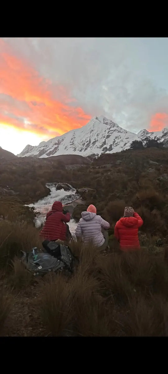 Three photographers facing a snowy peak under colourful clouds in Peru