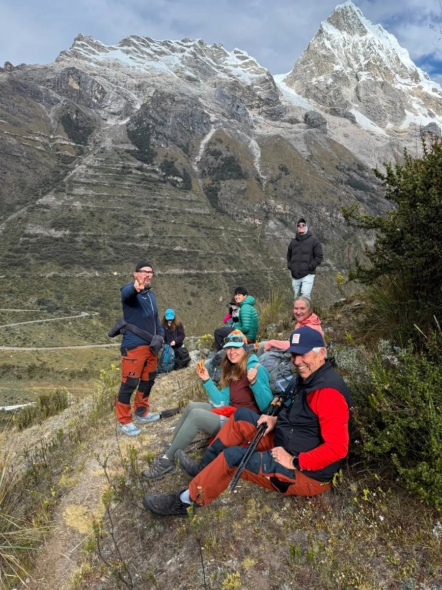 A photography group resting on a trail beneath snow-covered mountains in Peru