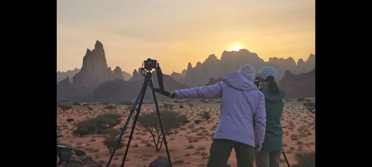 Two photographers with tripods overlooking sandstone formations in warm desert light in Saudi Arabia