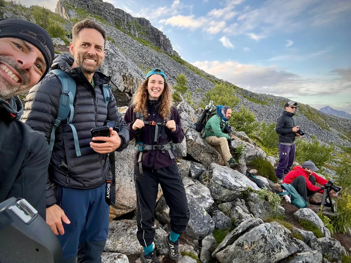 A smiling photography group taking a break on a rocky mountain trail on Senja