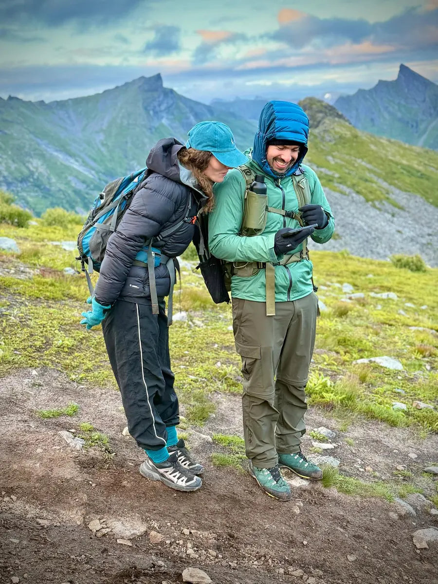 Two hikers looking at a camera together with green mountain ridges behind them on Senja