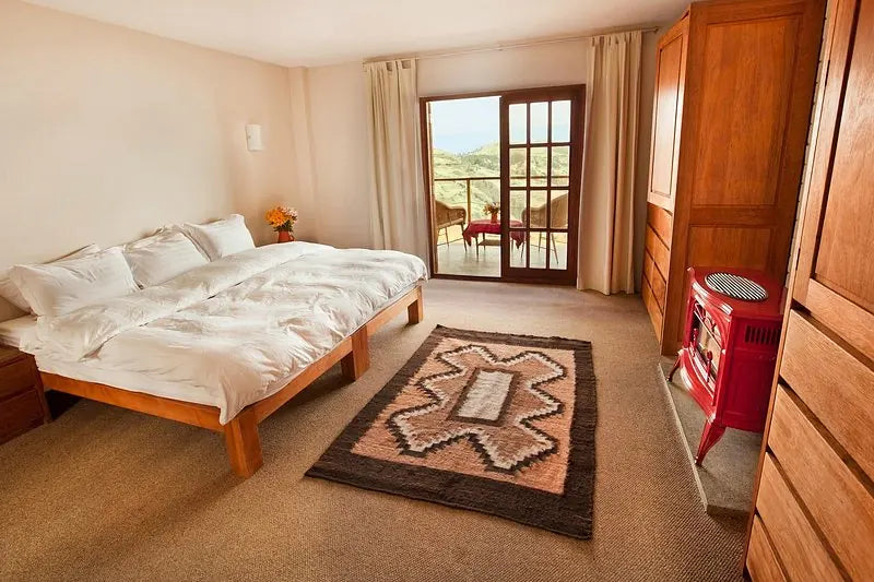 A mountain lodge bedroom with twin beds, a wood-burning stove and a balcony overlooking the landscape