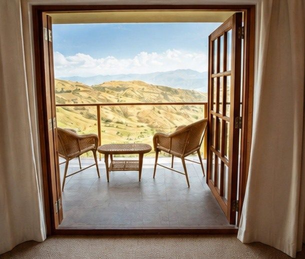 Open lodge doors leading to a balcony with chairs and views across the Peruvian Andes.