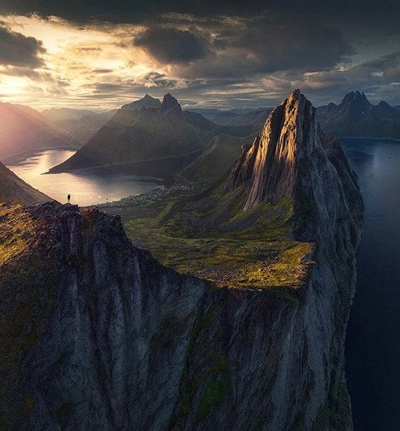 Segla and surrounding fjords in low golden light, with a small figure on the foreground ridge.