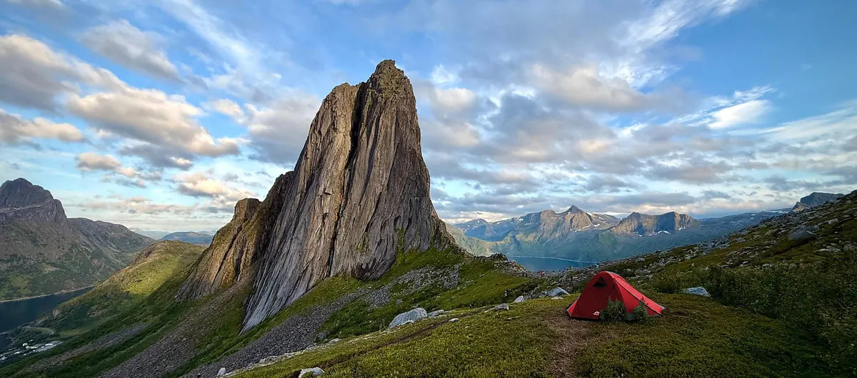 A red tent beside a dramatic rocky peak with fjords and mountains beyond on Senja