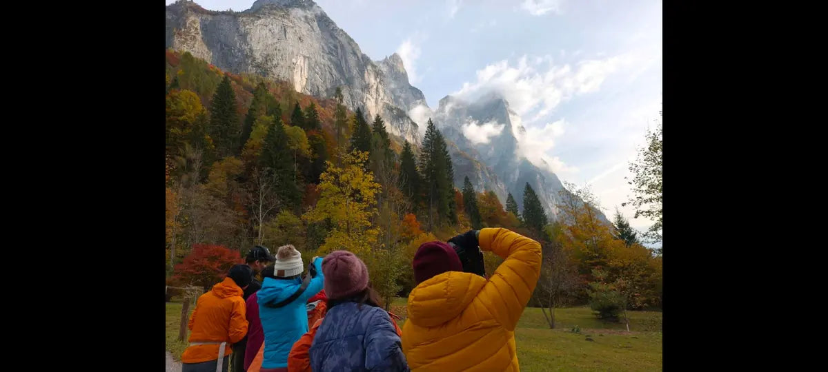 A group photographing autumn trees below a towering rock face