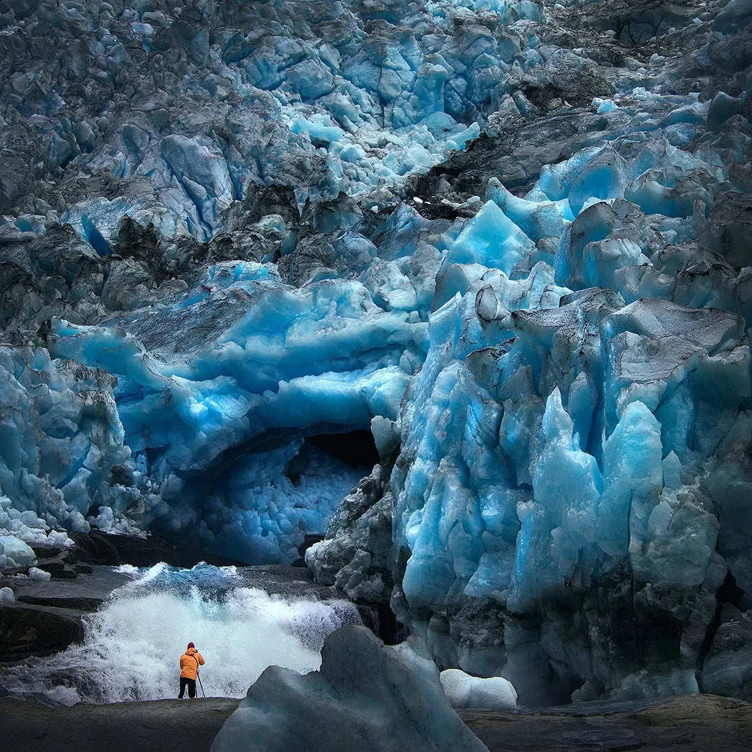A person beside a waterfall beneath towering blue glacial ice