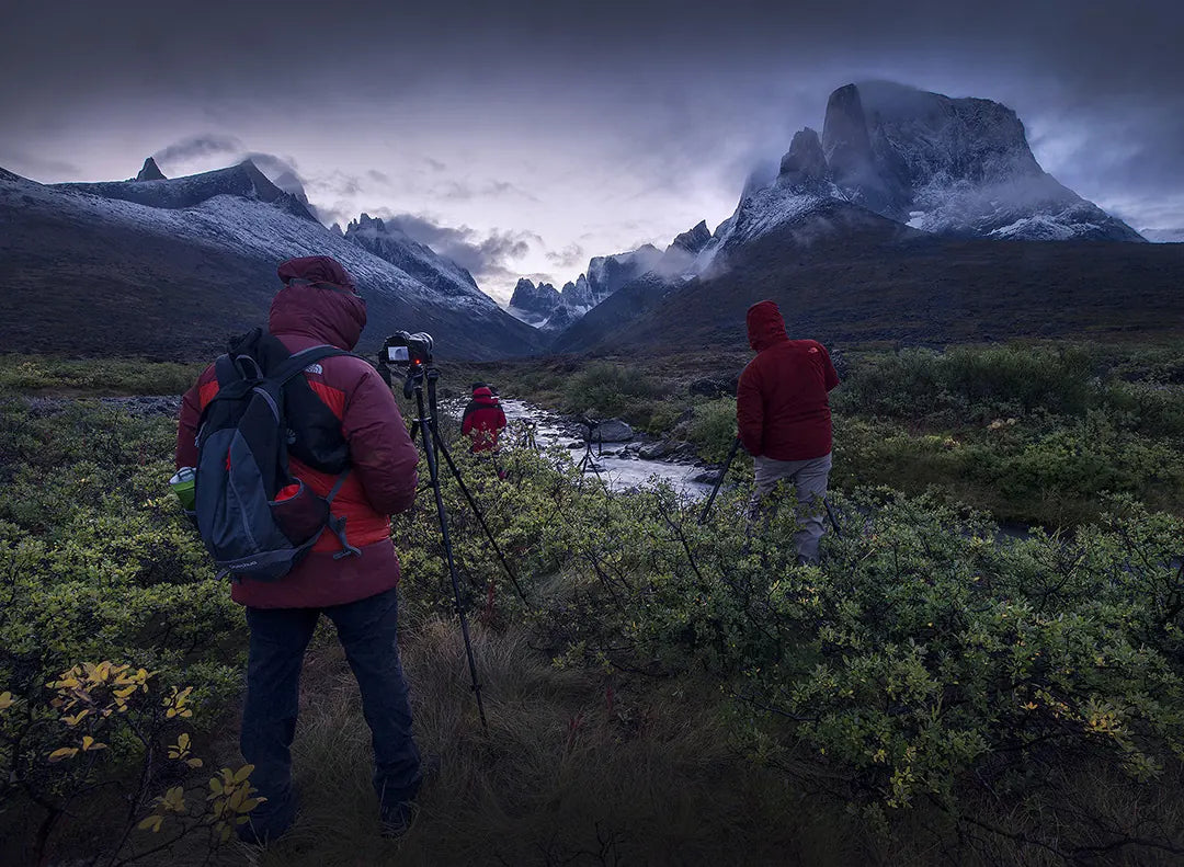 Photographers with backpacks and tripods in a green mountain valley beneath a moody sky