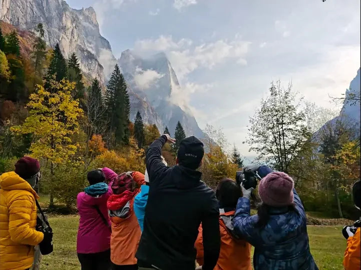 A photography group looking up at mountain cliffs surrounded by autumn trees