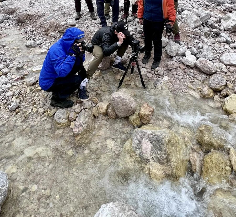 Photographers crouching beside a rocky stream to compose a photograph