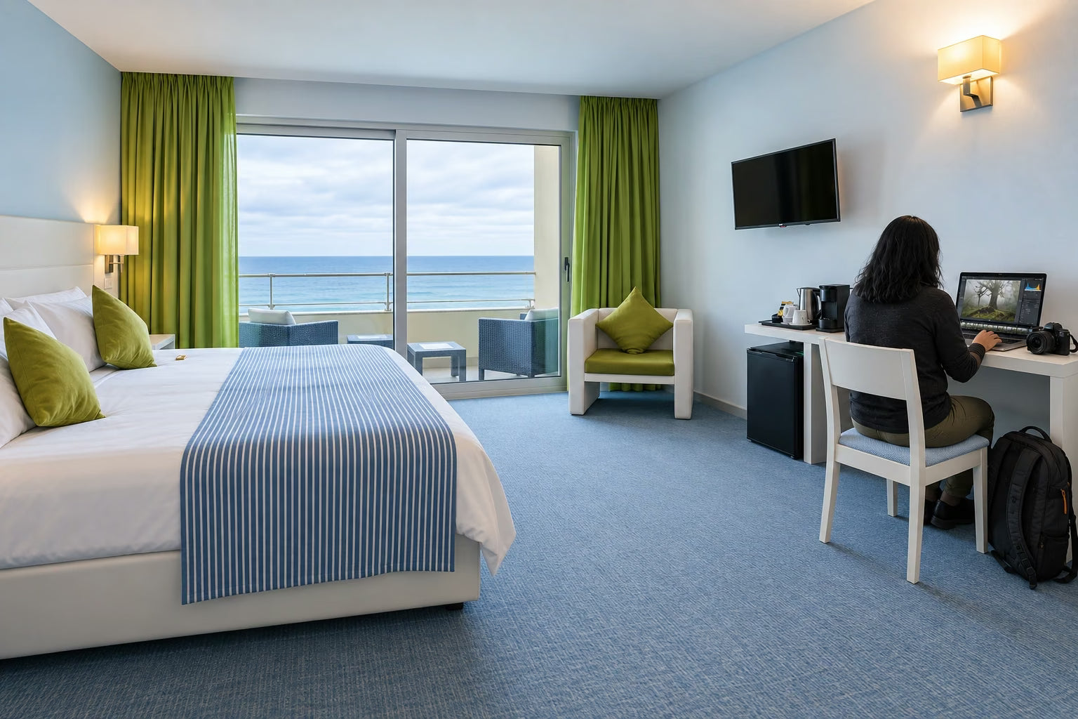 A photographer editing on a laptop in a spacious Madeira hotel room with an ocean-view balcony