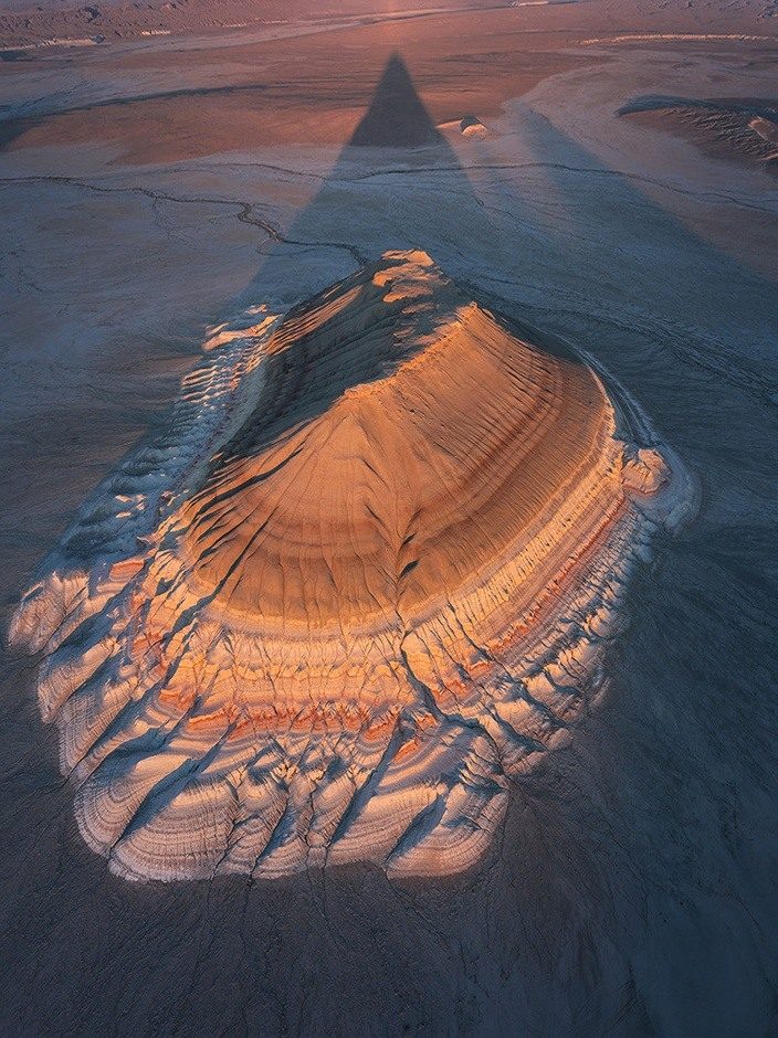 A flat-topped desert hill with layered slopes and a long shadow, seen from above in Mangystau.