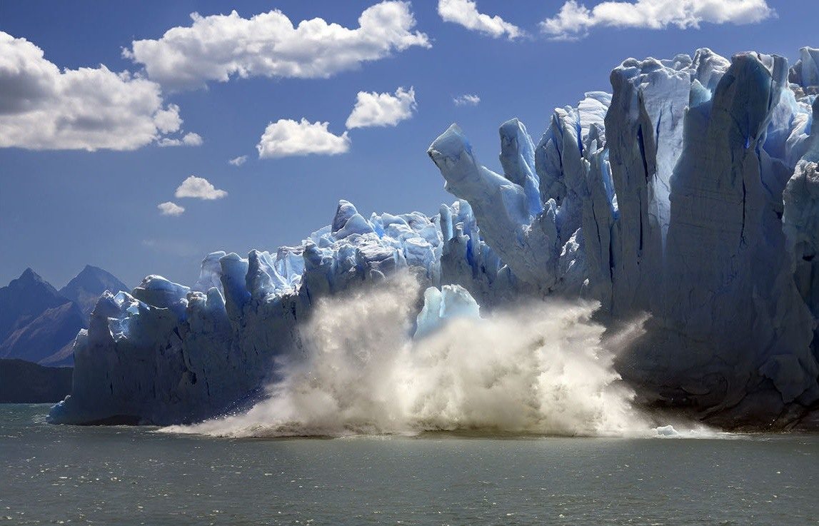 Ice breaking from a blue glacier wall into a lake in Patagonia.