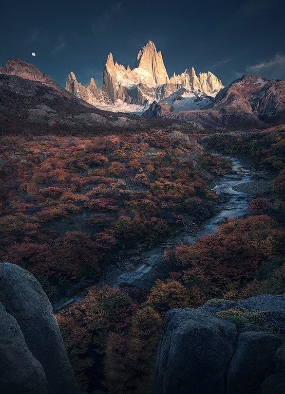 Fitz Roy glowing above autumn woodland and a winding stream, with a crescent moon overhead.