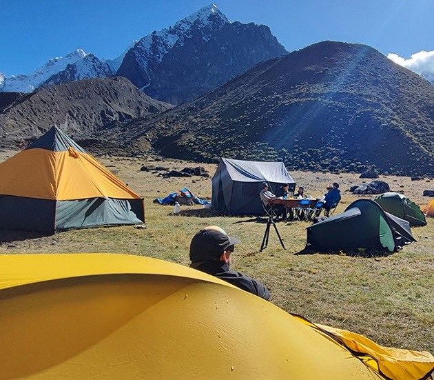 Tents and an outdoor dining area at a campsite beneath the mountains of the Peruvian Andes.